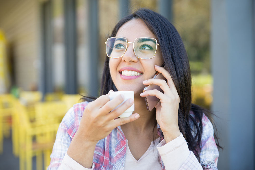 Positive smart student girl enjoying nice phone talk in street coffee shop