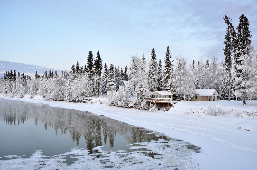 Winter River in Alaska with forest and buildings reflected in the water