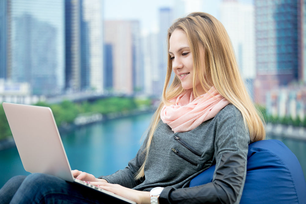Young girl using laptop study working communicating ordering online sitting in comfortable beanbag chair cityscape on the background