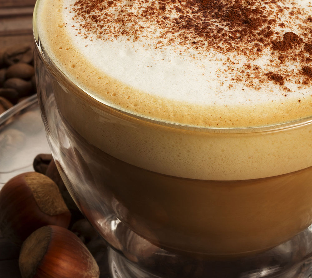 cappuccino with chocolate powder on milk froth and hazelnuts on wooden background