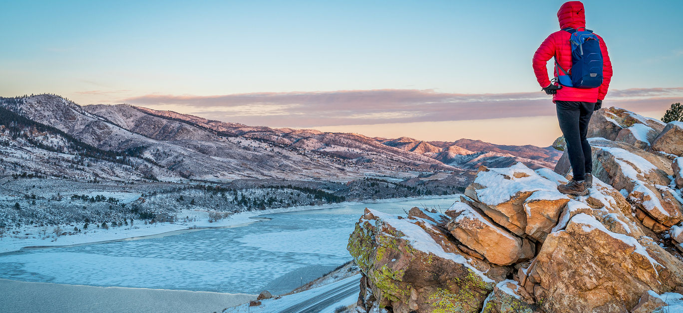 male hiker contemplating winter sunrise over frozen Horsetooth Reservoir at Rocky Mountains foothills near Fort Collins, Colorado