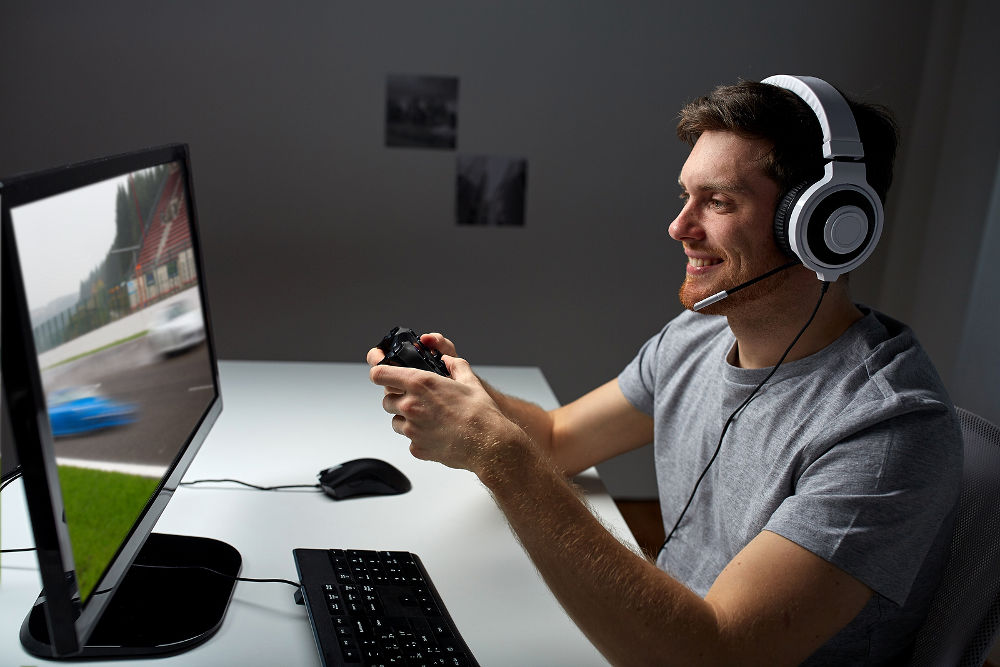 happy young man in headset with controller gamepad playing computer game at home