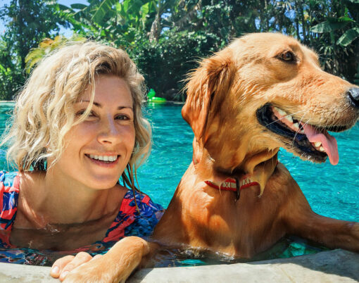 Funny portrait of smiling woman relaxing with golden retriever puppy in tropical swimming pool
