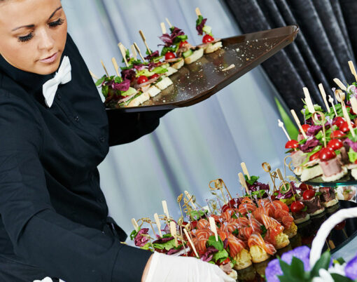 Waiter with meat dish serving catering table with food snacks during party event