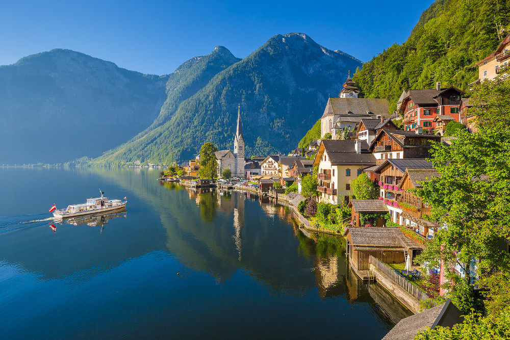 Scenic picture-postcard view of famous Hallstatt mountain village in the Austrian Alps with passenger ship in beautiful morning light on a sunny day in summer Salzkammergut region Austria