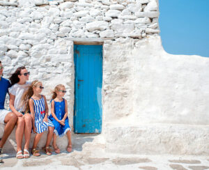 Family vacation in Europe. Parents and kids at street of typical greek traditional village with white walls and colorful doors on Mykonos Island, in Greece