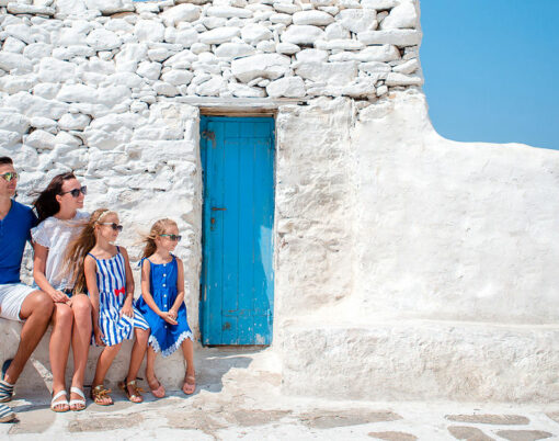 Family vacation in Europe. Parents and kids at street of typical greek traditional village with white walls and colorful doors on Mykonos Island, in Greece