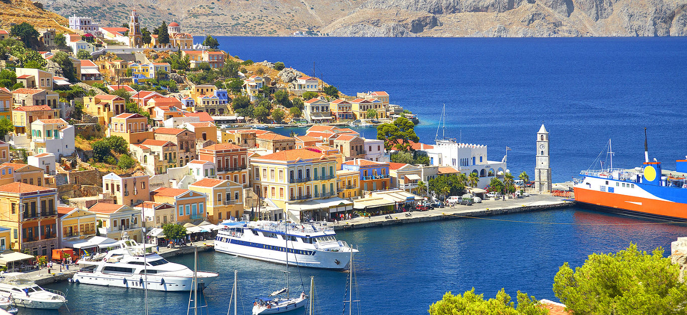 View on Greek sea Symi island harbor port, classical ship yachts, houses on island hills, tourists Aegean Sea bay. Greece islands holidays vacation travel tours from Rhodos island. Greece architecture