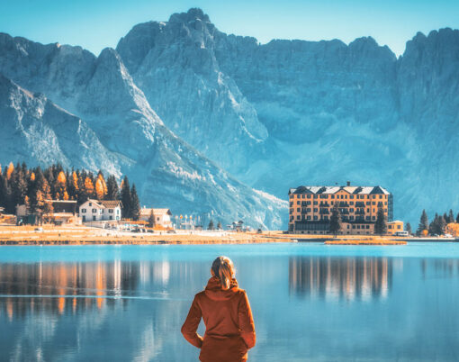 Young woman standing on the coast of Misurina lake at sunrise in autumn. Dolomites, Italy